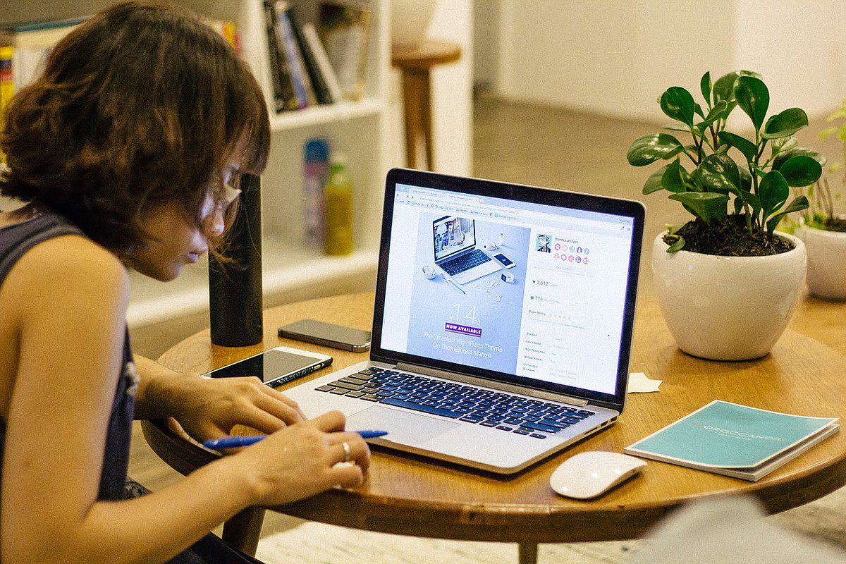 woman writing down informations displayed on laptop screen